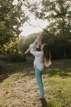 A mother joyfully lifts her baby in a sunny park setting, capturing a tender moment.
