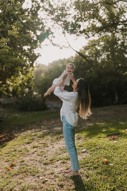 A mother joyfully lifts her baby in a sunny park setting, capturing a tender moment.