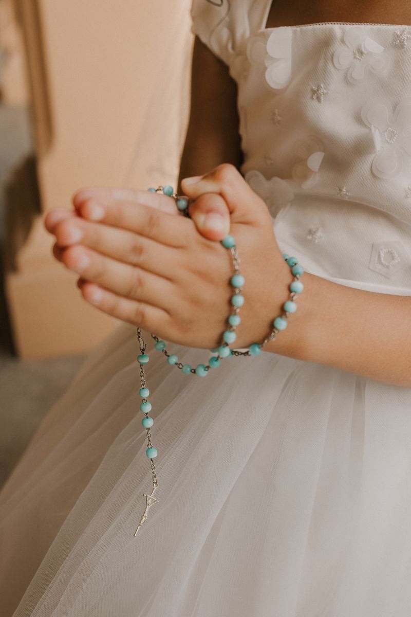 Small child's hands folded in prayer holding rosary beads