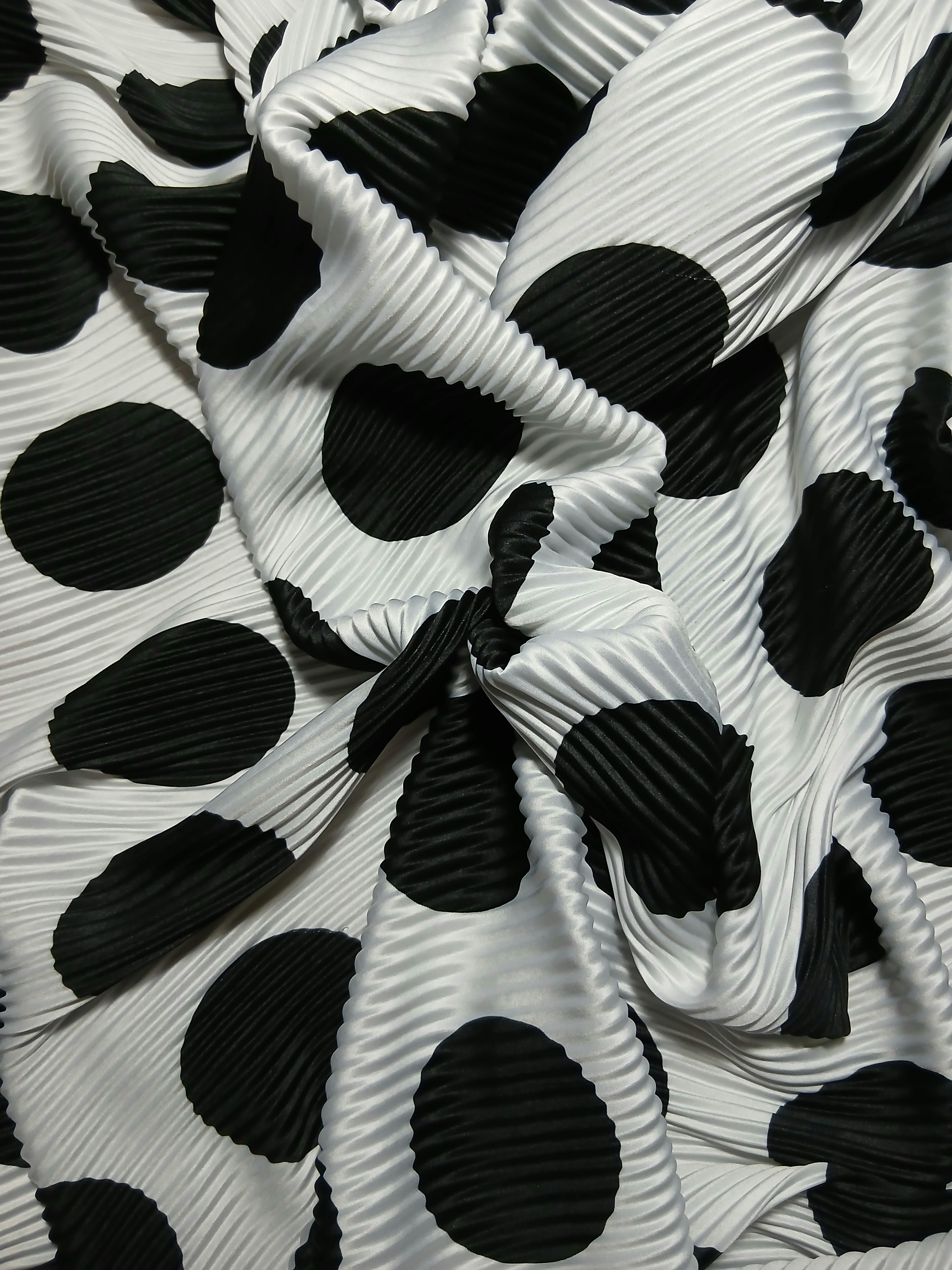 Artistic close-up of a pleated fabric with black polka dots on white background.