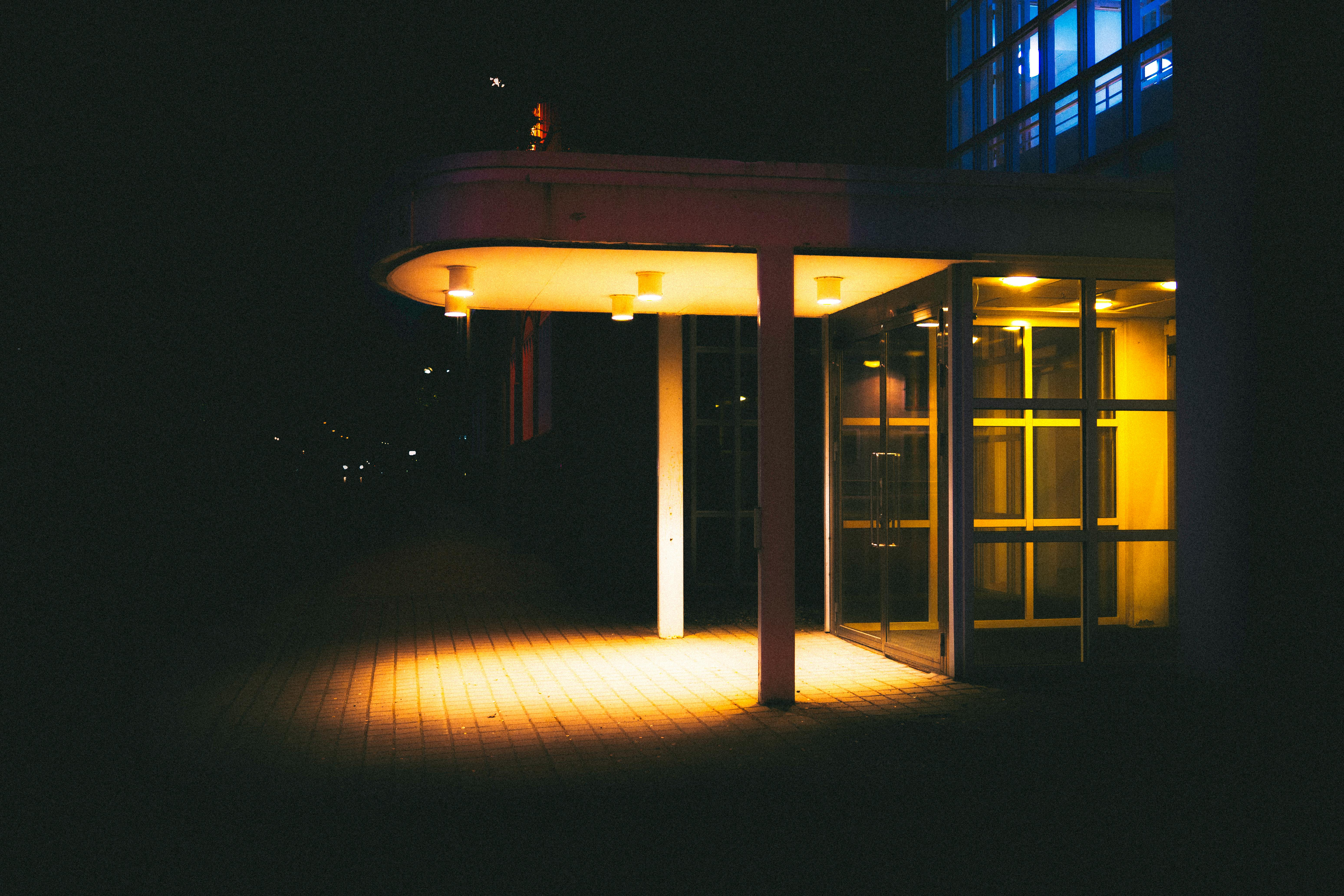 Ücretsiz Sıcak ve parlak ışıklarla aydınlatılmış modern bir binanın girişinin gece fotoğrafı. Stok Fotoğraflar