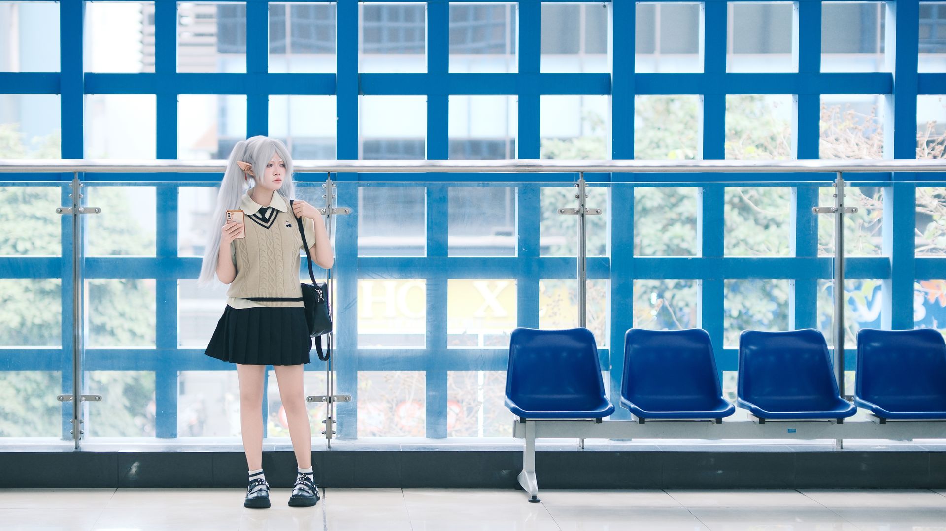 Teen girl in cosplay with long white hair and ears, standing indoors near blue window.