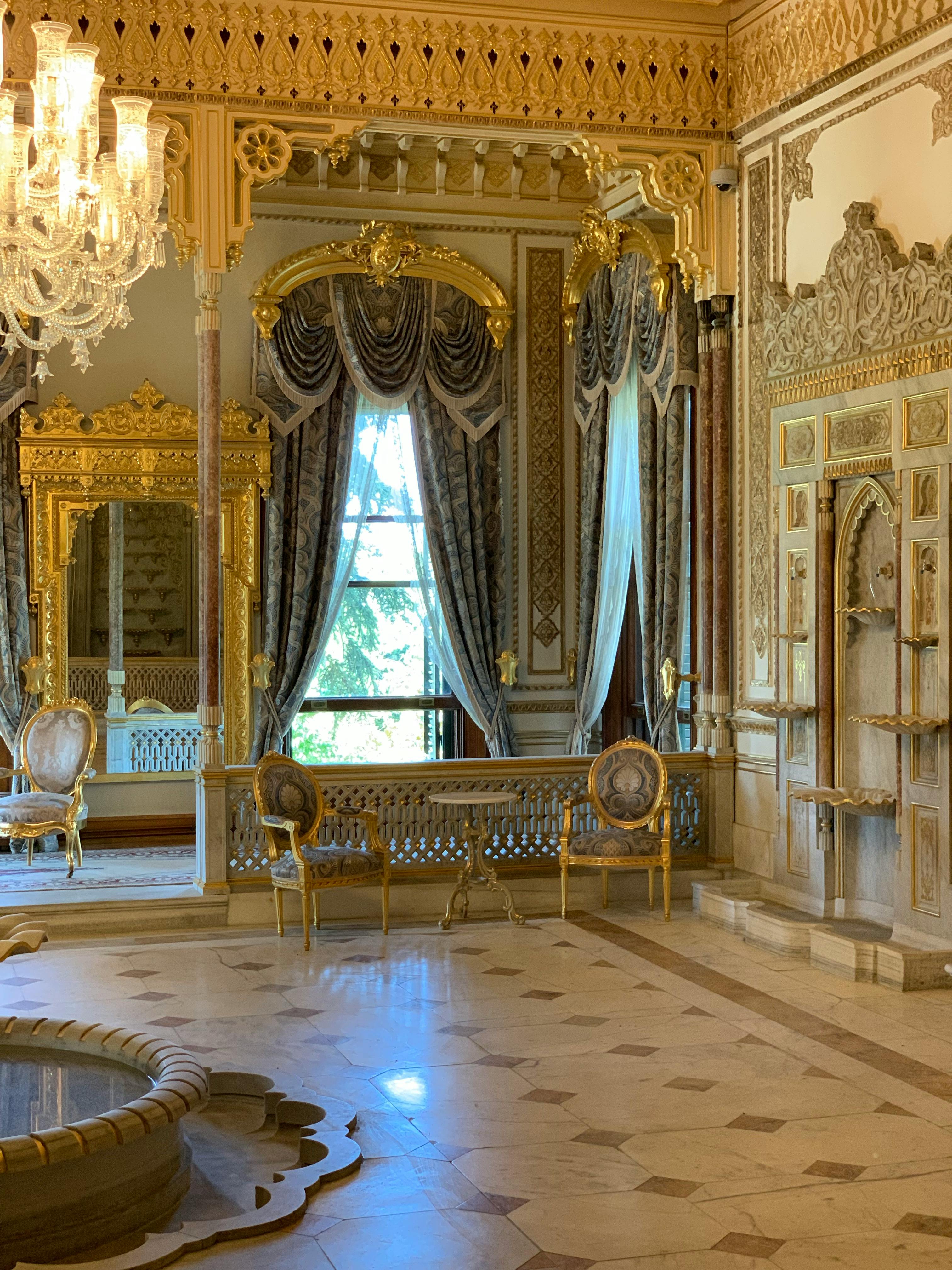 Luxurious neoclassical room with gold decor, chandelier, and large window.