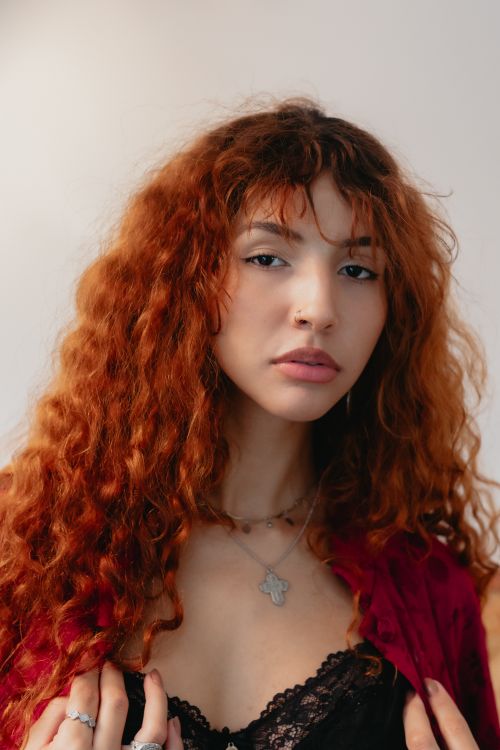 Free A confident woman with curly red hair poses indoors in São Paulo, Brazil. Stock Photo