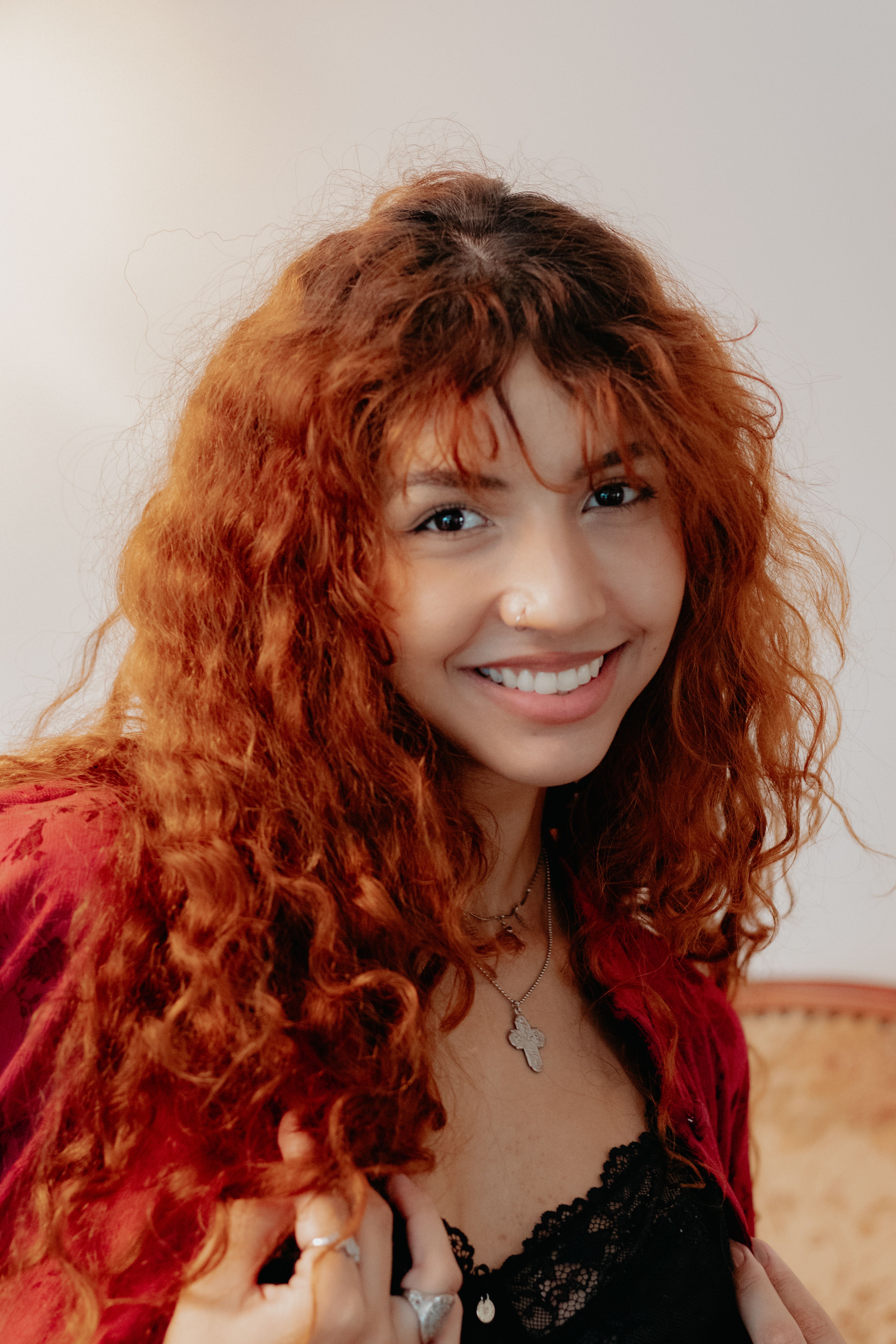 Bright portrait of a young woman with curly red hair and a joyful expression, indoors in São Paulo, Brazil.