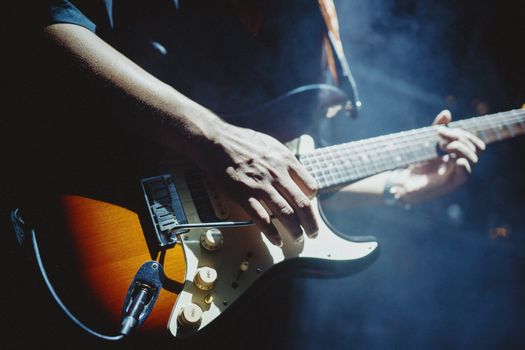 Close-up of a musician playing an electric guitar under stage lights, creating a vibrant atmosphere.