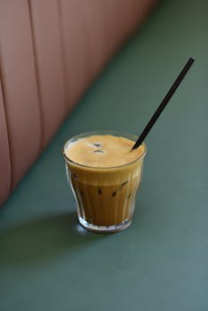 Foamy iced coffee in a glass with a straw on a green table, perfect summer refreshment.