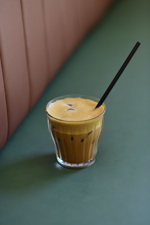 Free Foamy iced coffee in a glass with a straw on a green table, perfect summer refreshment. Stock Photo