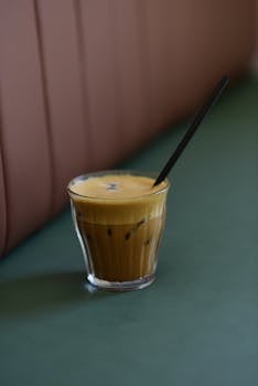 Refreshing iced coffee with a straw, served in a glass on a green table, perfect for a cozy coffee shop vibe.