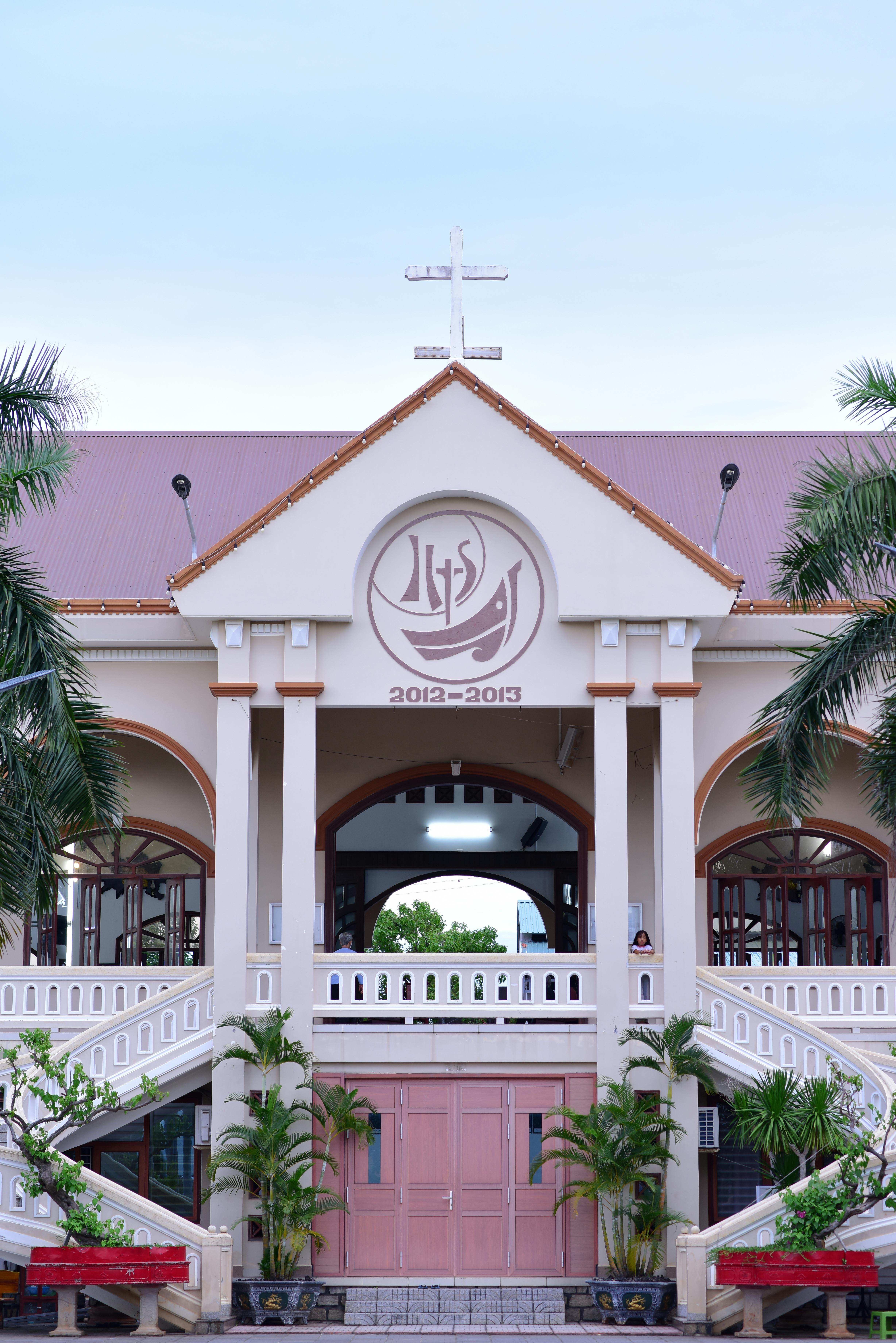 Front view of a church facade with palm trees and clear sky, ideal for religious or architectural themes.