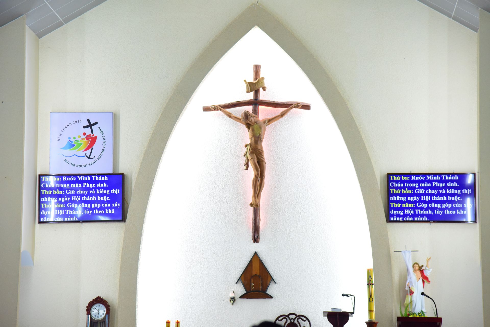 A serene church interior with a crucifix, flanked by digital screens displaying religious text.