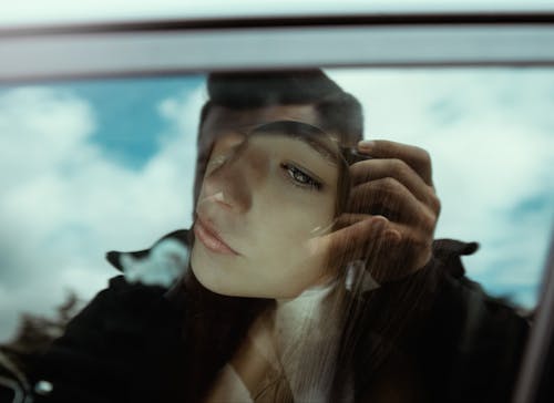 Unrecognizable man taking photo of pensive young female sitting in car and looking through window
