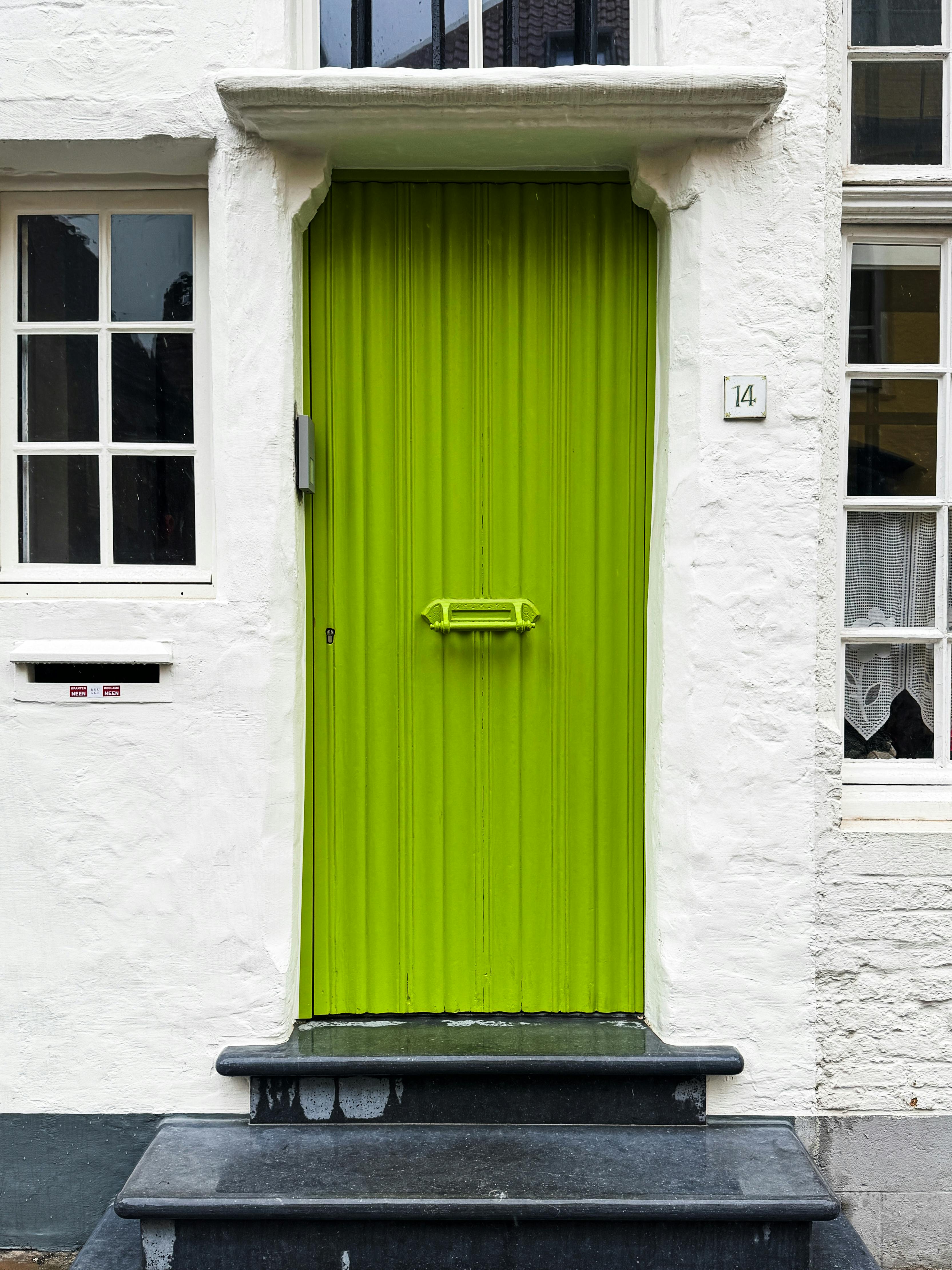 A striking lime green door on a historic building facade in Bruges, Belgium.