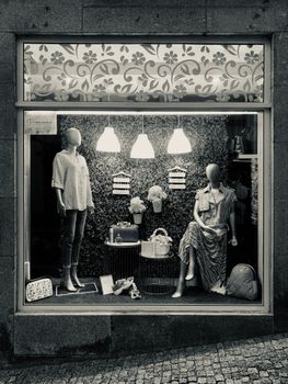 Black and white photo of a stylish fashion window display with mannequins and decor.