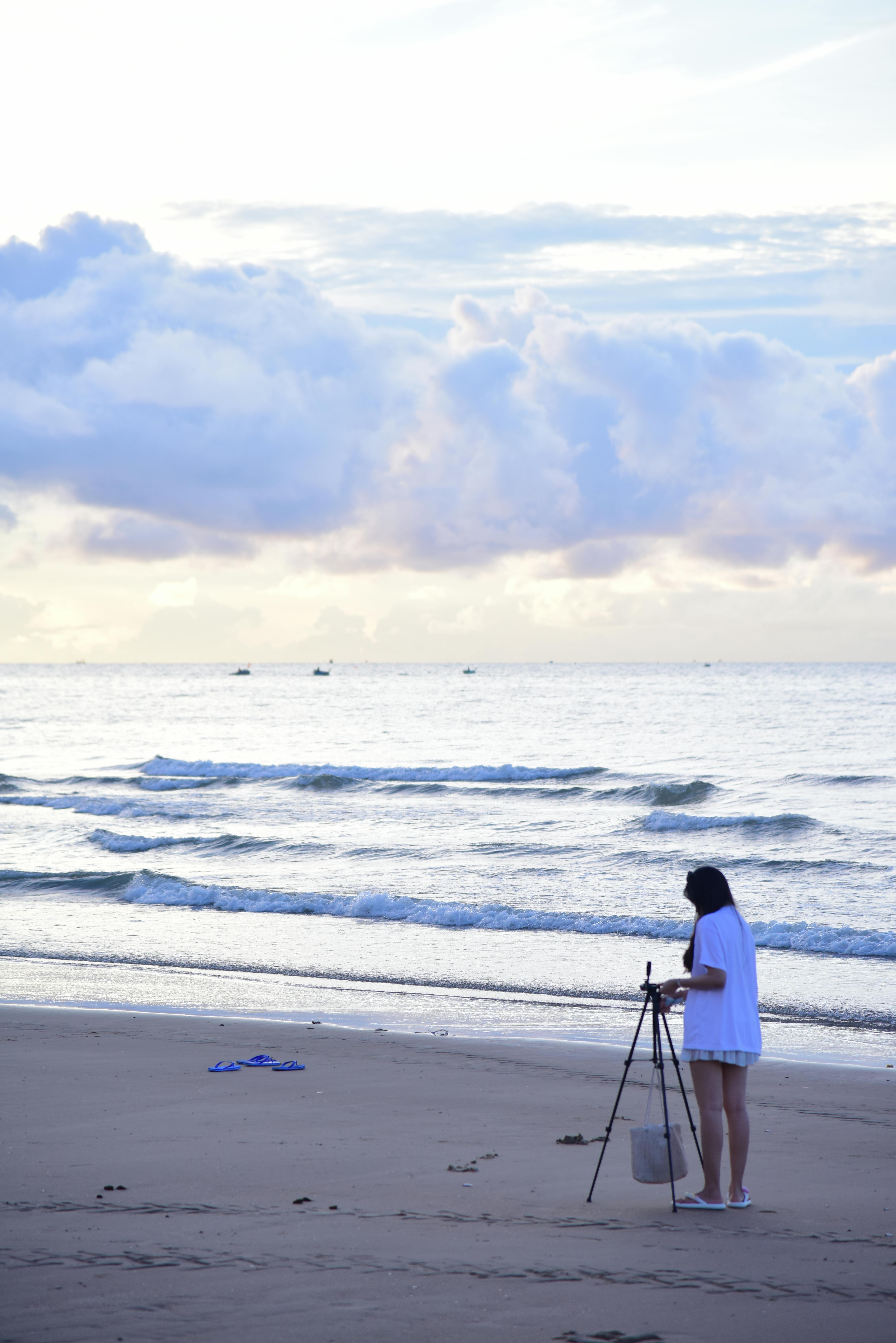 A person sets up a tripod on a beach at sunrise, capturing the serene ocean view.