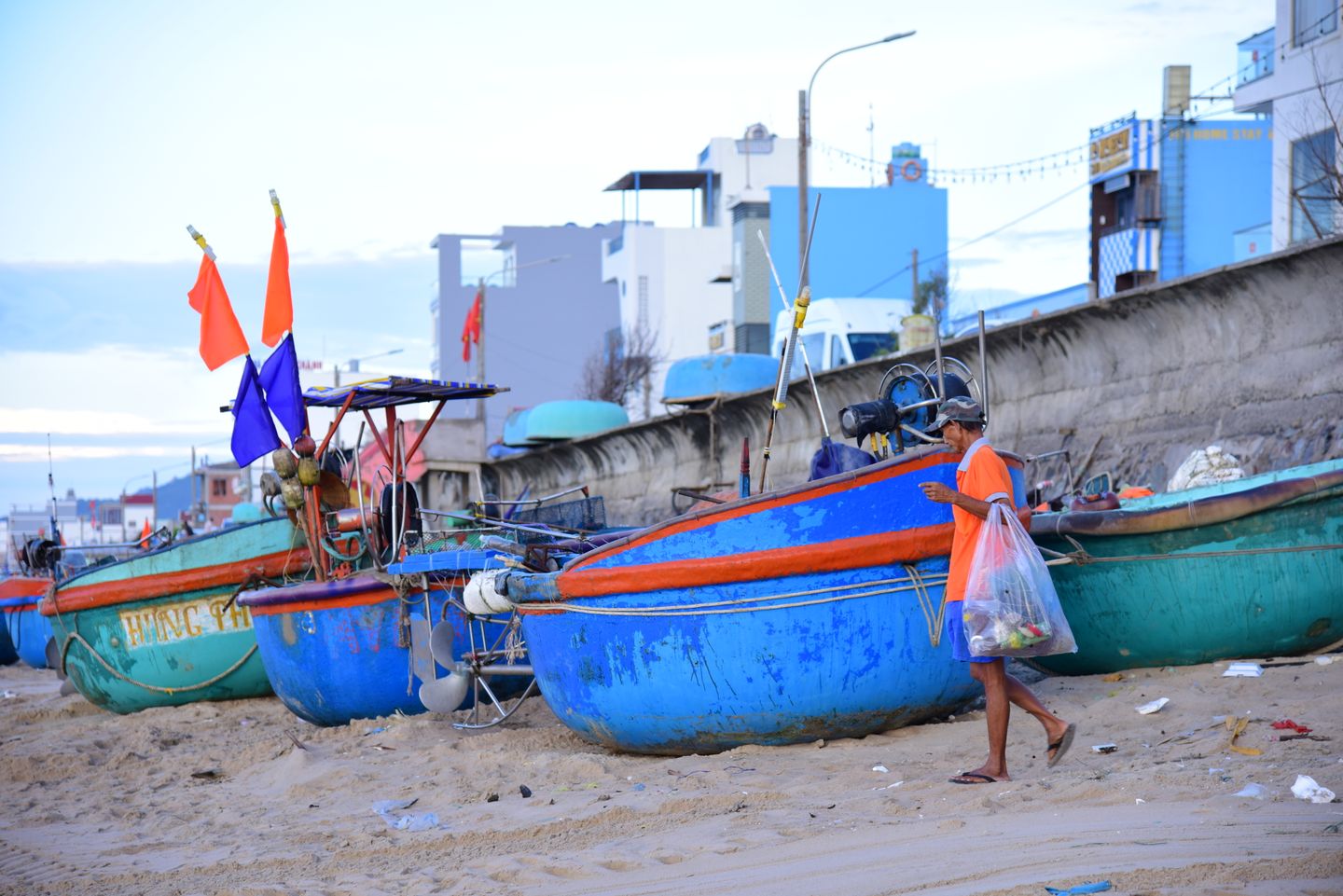 Fisherman walking past colorful boats on a beach in central Vietnam