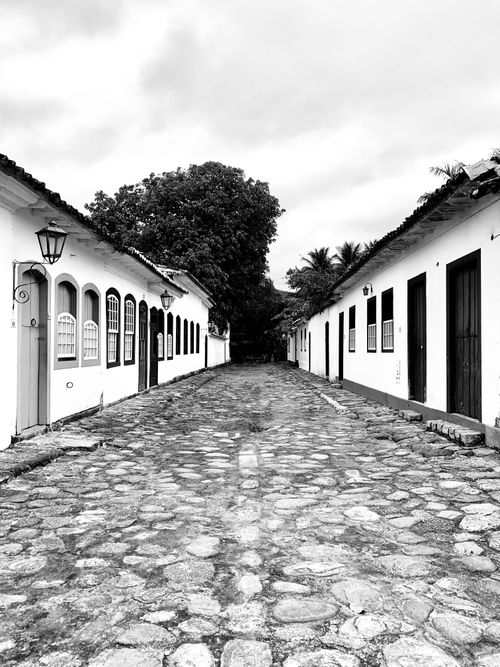 Free Black and white photo of a cobblestone street flanked by colonial architecture. Stock Photo