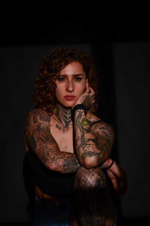 Free Portrait of a young tattooed woman with curly hair in a dramatic low-light studio setting. Stock Photo