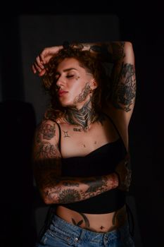 Captivating image of a tattooed young woman posing in a dimly lit studio, showcasing body art.