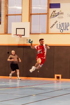 Action shot of a handball player jumping in an indoor sports arena in France.
