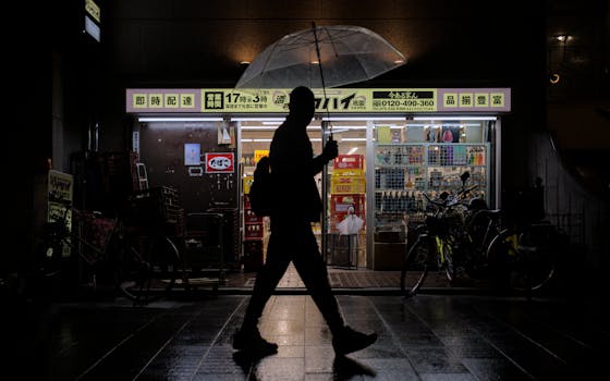 Nighttime scene in Kyoto with a person silhouetted against a shop, holding an umbrella in the rain.