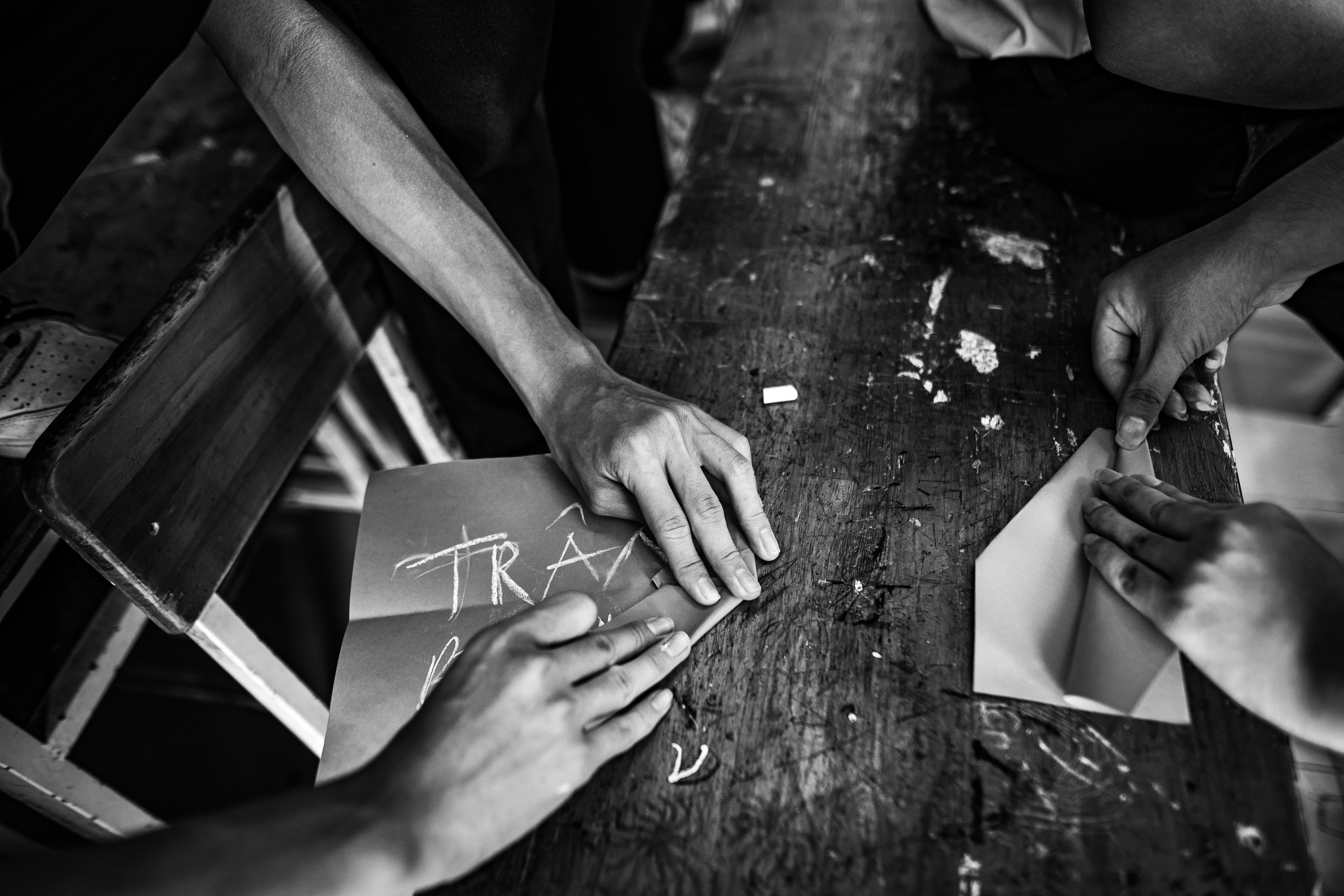 Black and white photo of hands crafting paper art on a rustic table, symbolizing teamwork and creativity.
