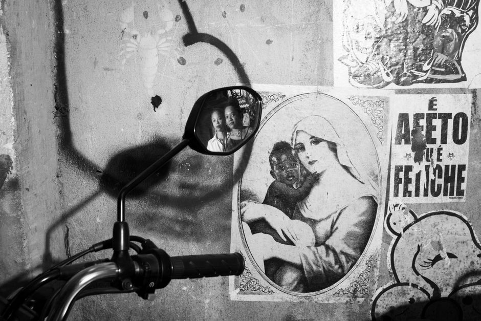 Monochrome street scene with a reflection in a motorcycle mirror capturing two adults against artistic graffiti.