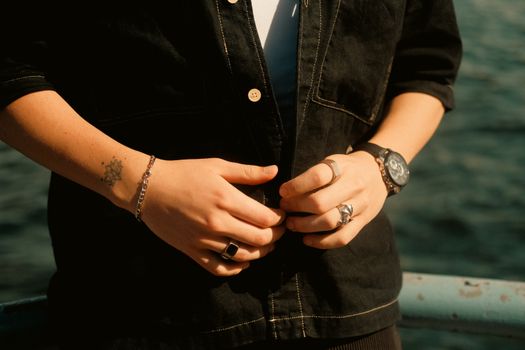 Detail shot of hands wearing rings, bracelet, and watch by the water.