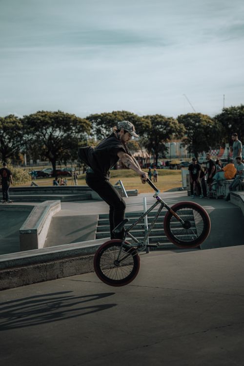 Free BMX rider performing a stunt at an outdoor skate park with an audience in the background. Stock Photo