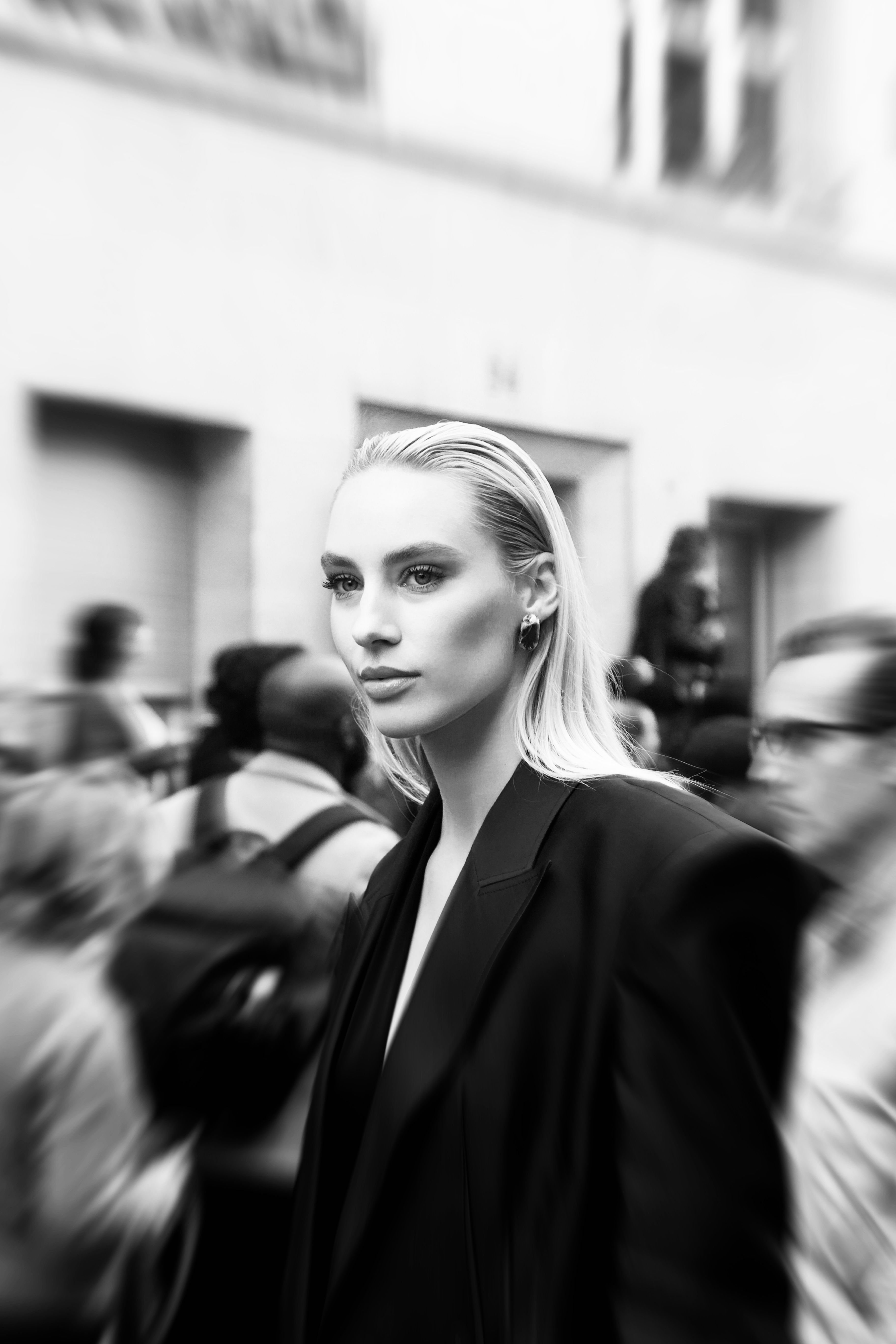 Stylish young woman in focus surrounded by a blurred Paris crowd, monochrome elegance.