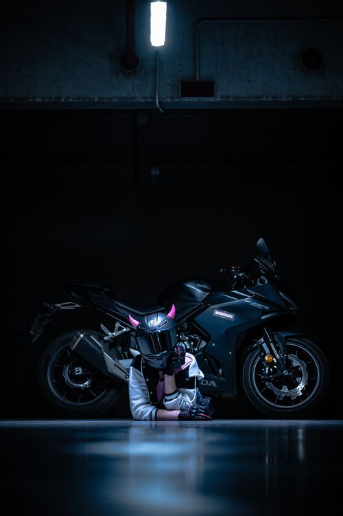 Free Motorcyclist with helmet poses near sleek black motorcycle in dimly lit garage. Stock Photo