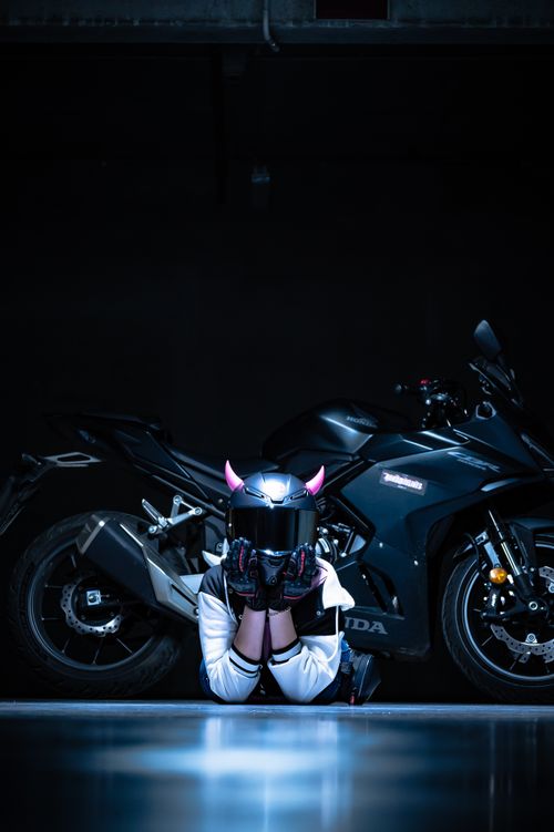 Free Motorcyclist kneeling by a sport bike in a dimly lit garage, helmet adorned with horns. Stock Photo