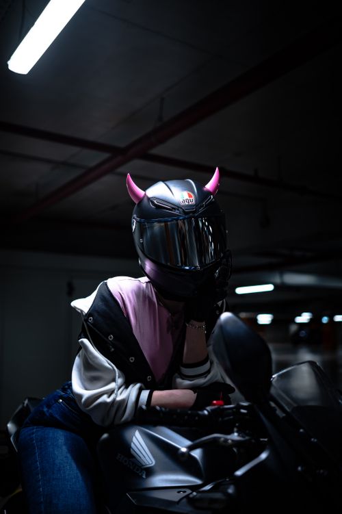 Free A biker with pink horns on helmet poses on a motorcycle in dimly lit garage. Stock Photo