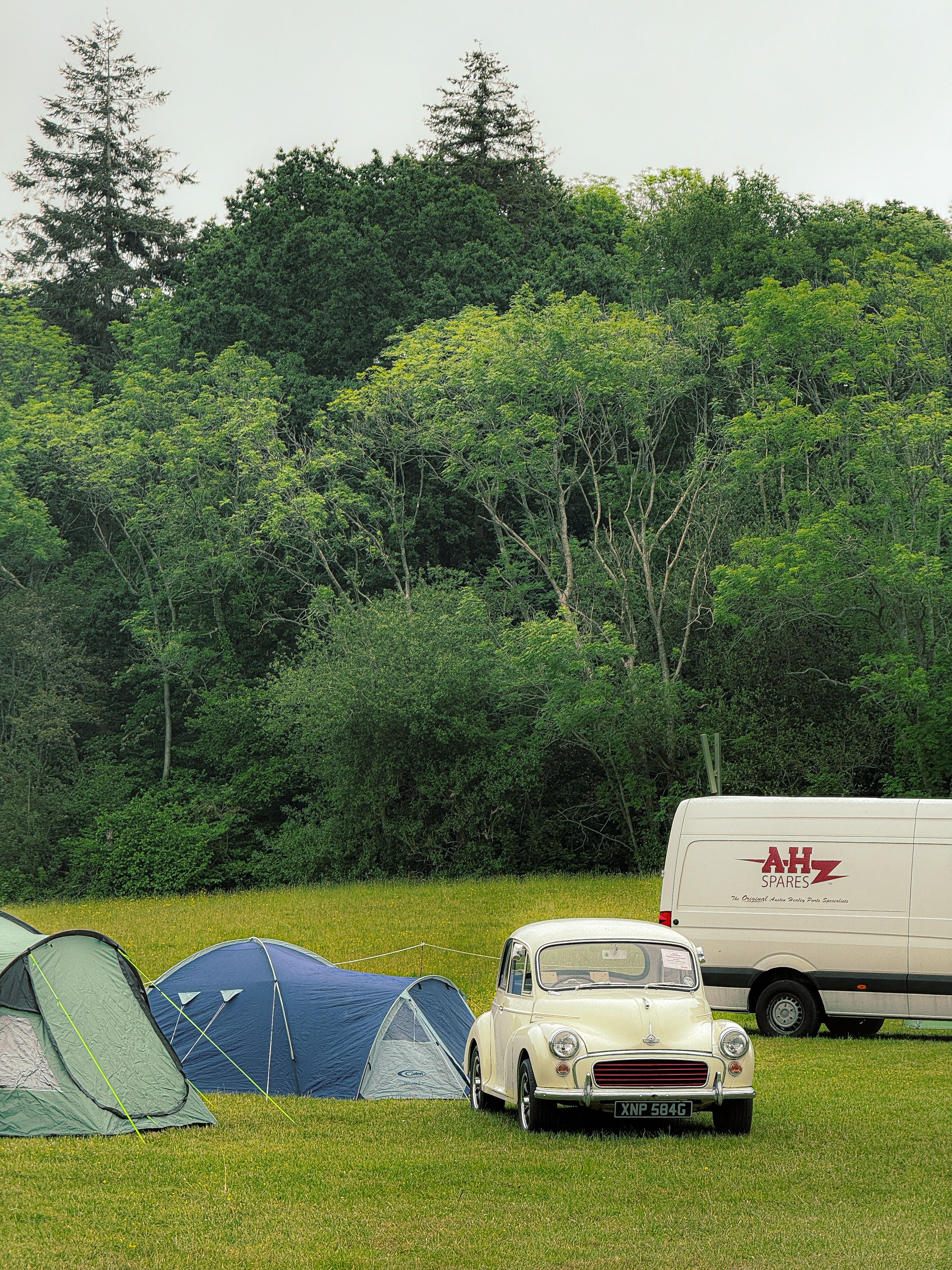 Scenic outdoor camping with tents and vintage car by a forest. Ideal for travel and adventure themes.