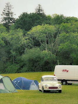 Scenic outdoor camping with tents and vintage car by a forest. Ideal for travel and adventure themes.