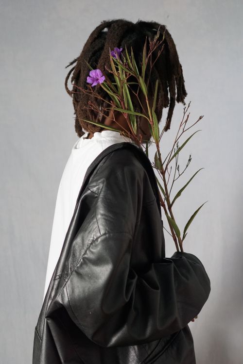 Free Stylish person in black jacket holding purple flowers against neutral background. Stock Photo