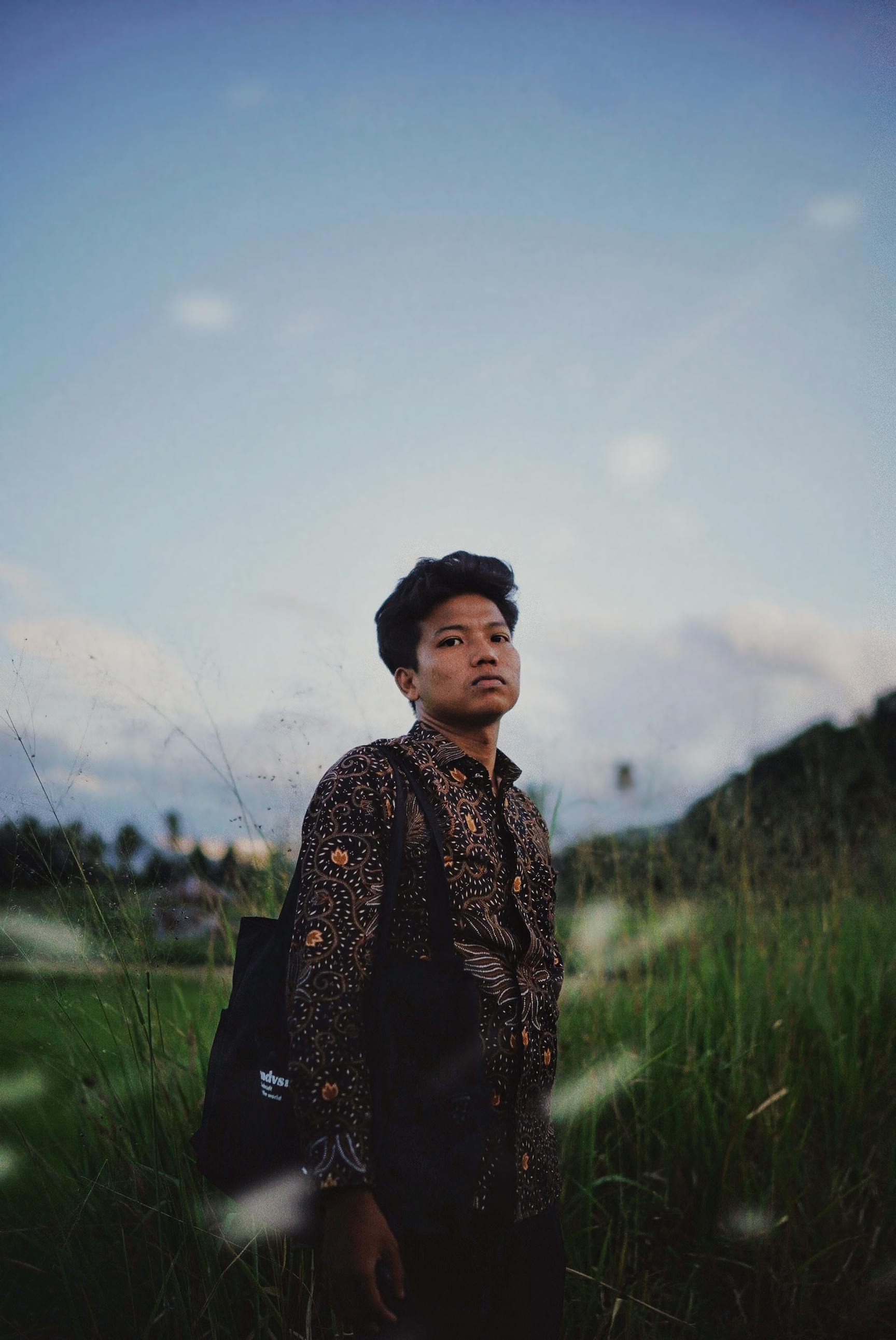 Portrait of a young man wearing traditional clothing in a grassy outdoor setting at sunset.
