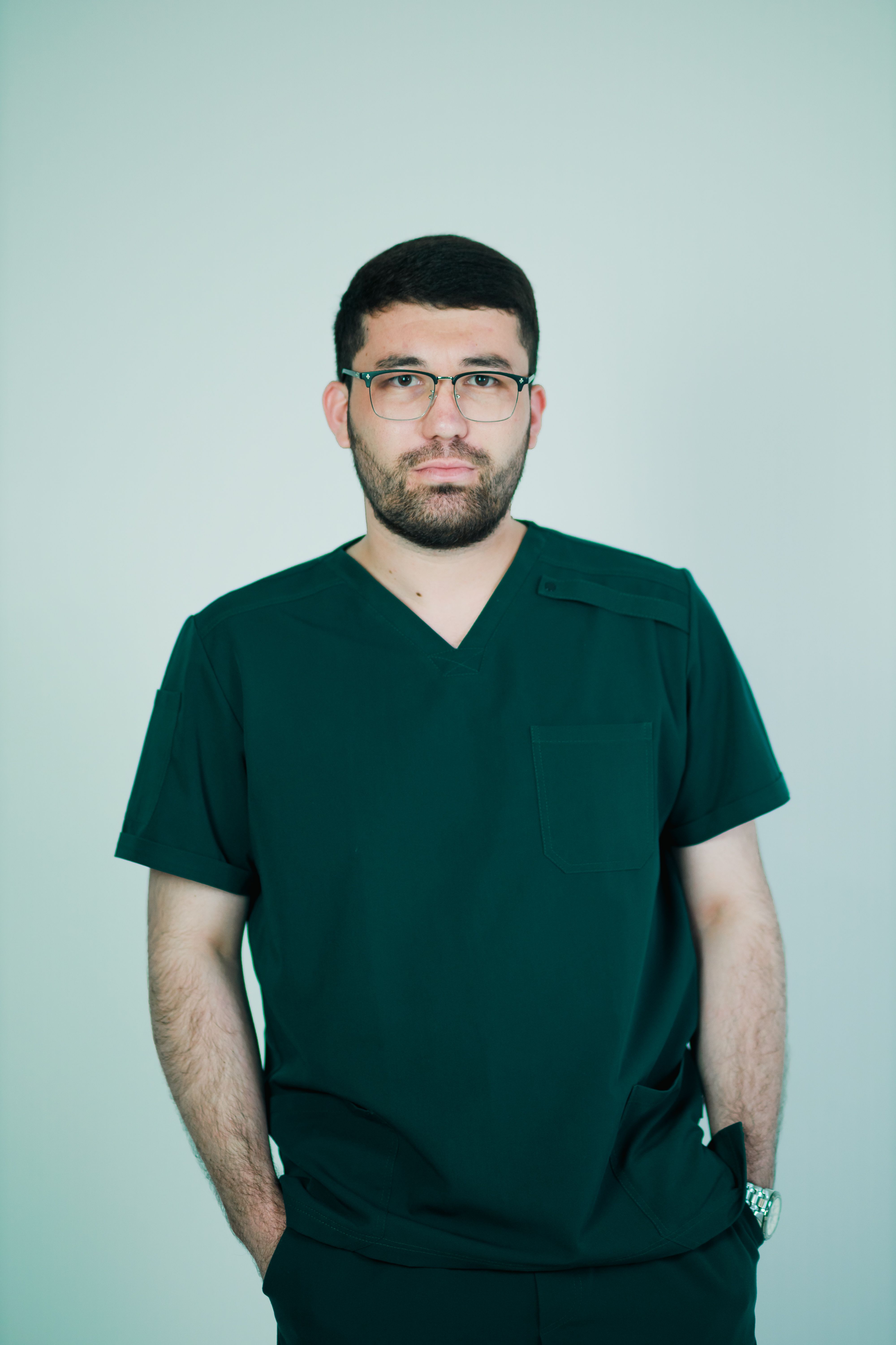 Male nurse in green scrubs poses confidently with a neutral background.