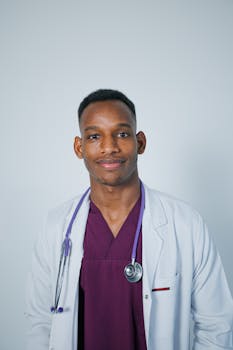 Smiling young doctor in a white coat and purple scrubs, looking confident and approachable.