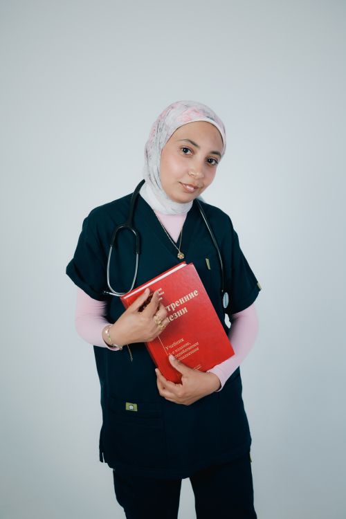 Free Young female doctor wearing hijab with a stethoscope and medical book, portraying professionalism. Stock Photo