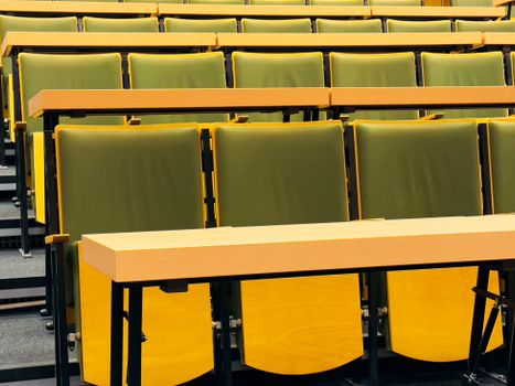 Modern lecture hall with green folding chairs and wooden desks. Ideal for educational spaces.