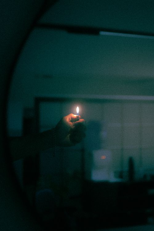 Free A mysterious, dimly lit room with a hand holding a lit lighter, casting a warm glow. Stock Photo