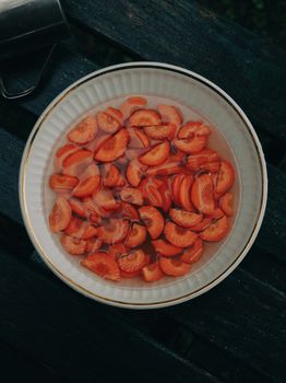 A bowl filled with sliced carrots soaking in water, placed on rustic wooden planks.