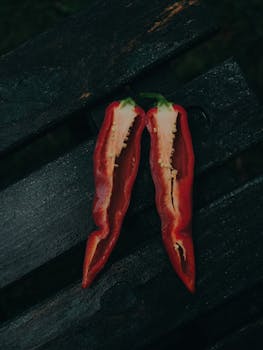 High-contrast image of a sliced red bell pepper resting on dark wooden boards, creating a moody, rustic vibe.