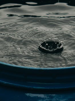 Close-up of a water droplet creating a splash in a blue barrel, capturing the motion in detail.