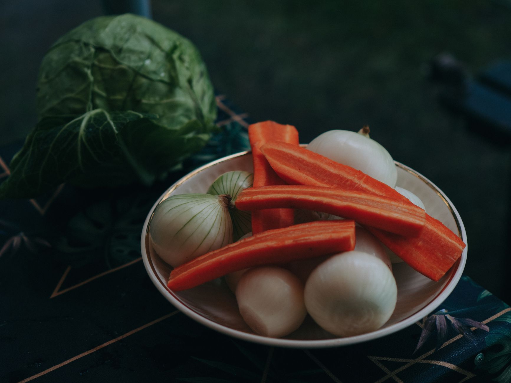 旅行鍋做晚餐加菜不費力:10分鐘簡單上桌 Bowl of fresh carrots and onions with cabbage on a dark, patterned tablecloth outdoors.