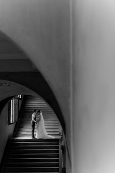Bride and groom share a kiss on stairs in a classic black and white setting.