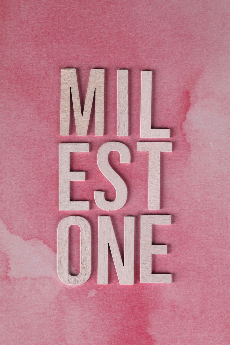 Wooden letters spelling 'Milestone' on a pink watercolor backdrop, symbolizing achievement.