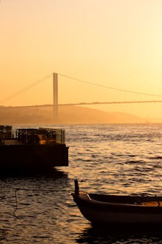 Captivating view of Bosphorus Bridge at sunset, with a calm sea and boat silhouette.