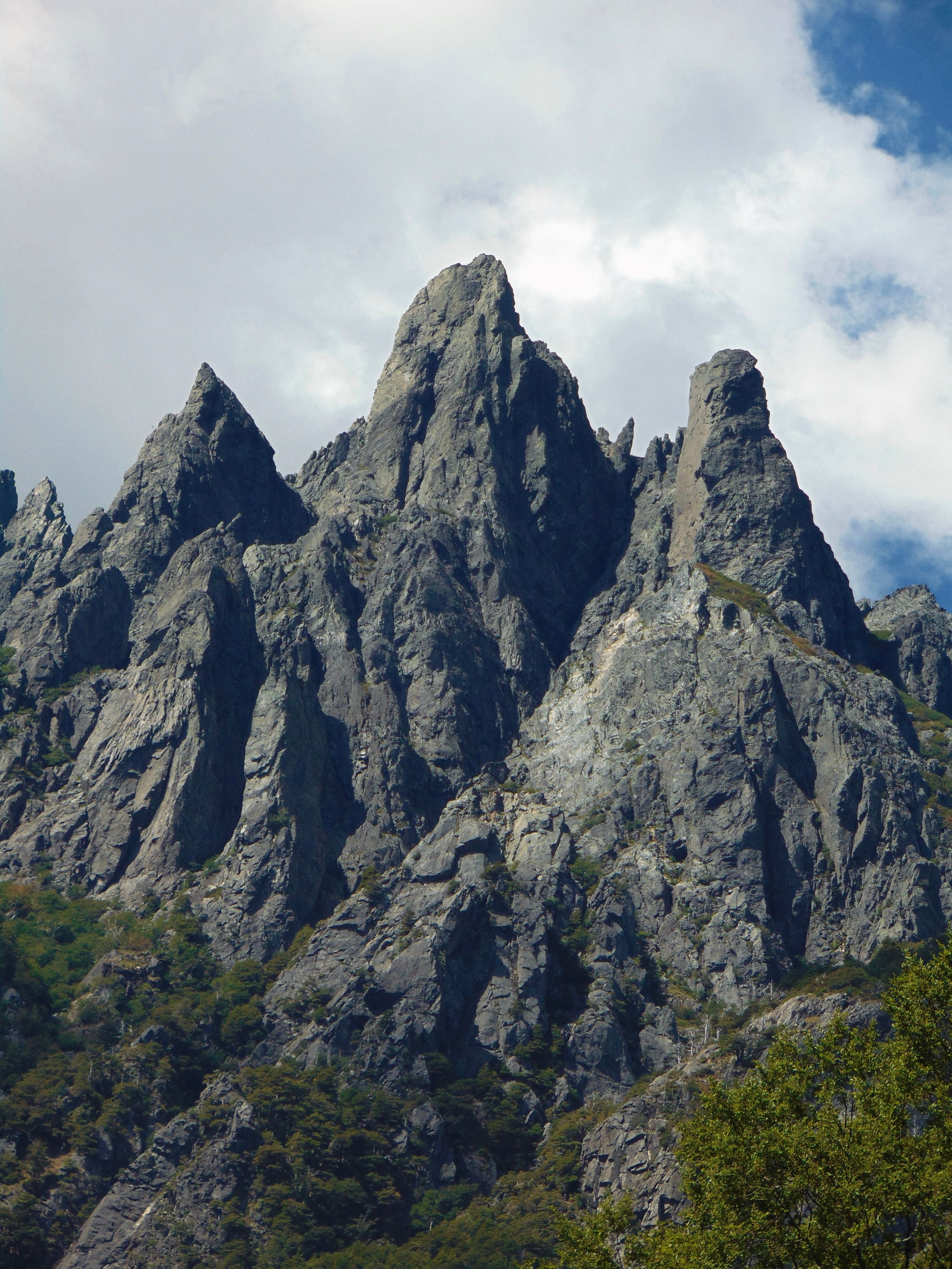Dramatic rocky mountain peaks rising against a bright cloudy sky, showcasing natural geological formations.